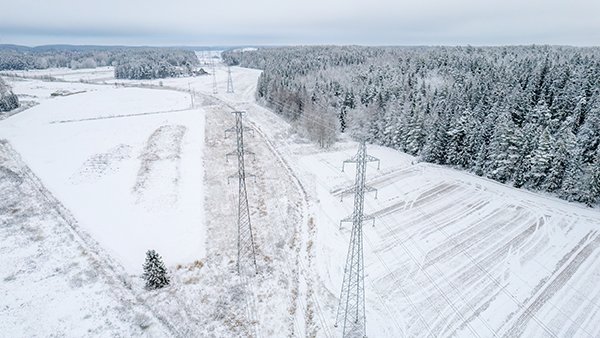 Ilmakuva, jossa sähköjohto kulkee lumisten puiden ja lumisten peltojen läpi kylmänä pakkaspäivänä Suomessa. 