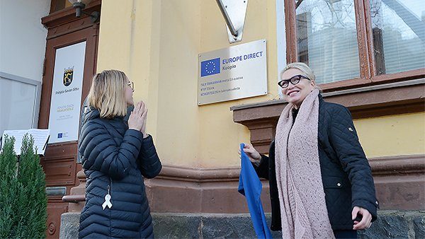 Kaksi henkilöä paljastavat seinään kiinnitetyn kyltin