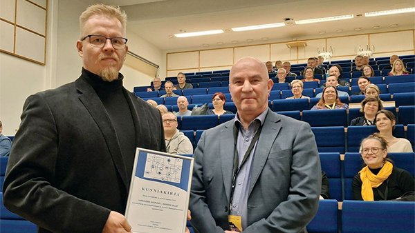 Kaksi miestä yleisön edessä kunniakirja käsissä