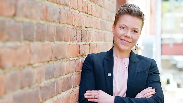 Henkilökuva Tytti Määtästä, joka nojaa tiiliseinään