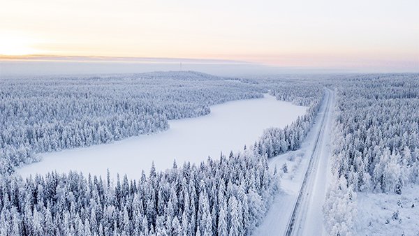 Jäätynyt järvi ja tie talvisessa metsämaisemassa