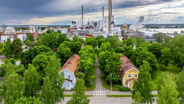 Kesäinen dronekuva, jossa taustalla tehtaat ja etualalla puutalot puiston keskellä